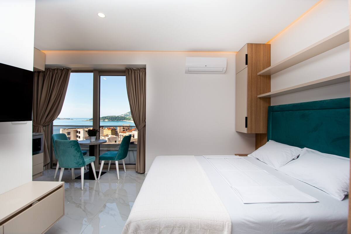 A hotel room with a bed, a desk, a chair, and a view of the sea.