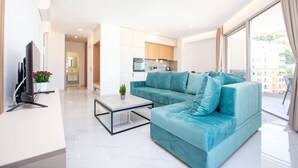 A modern living room with a teal sofa, a flat-screen TV, and a coffee table. - IN Property Apartments (Becici)