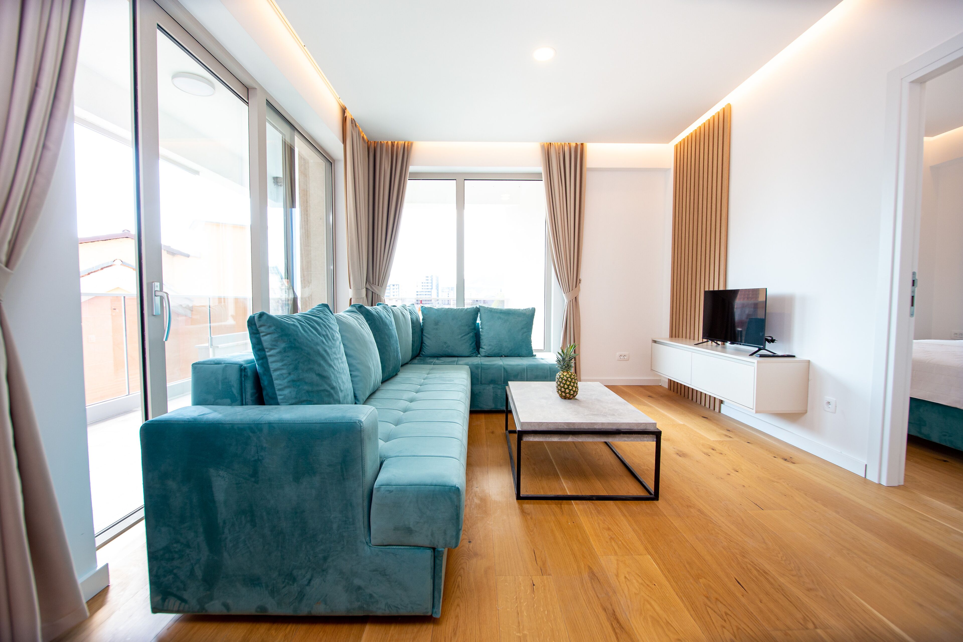 A modern living room with a teal sectional sofa, a coffee table, and a TV on a white cabinet.