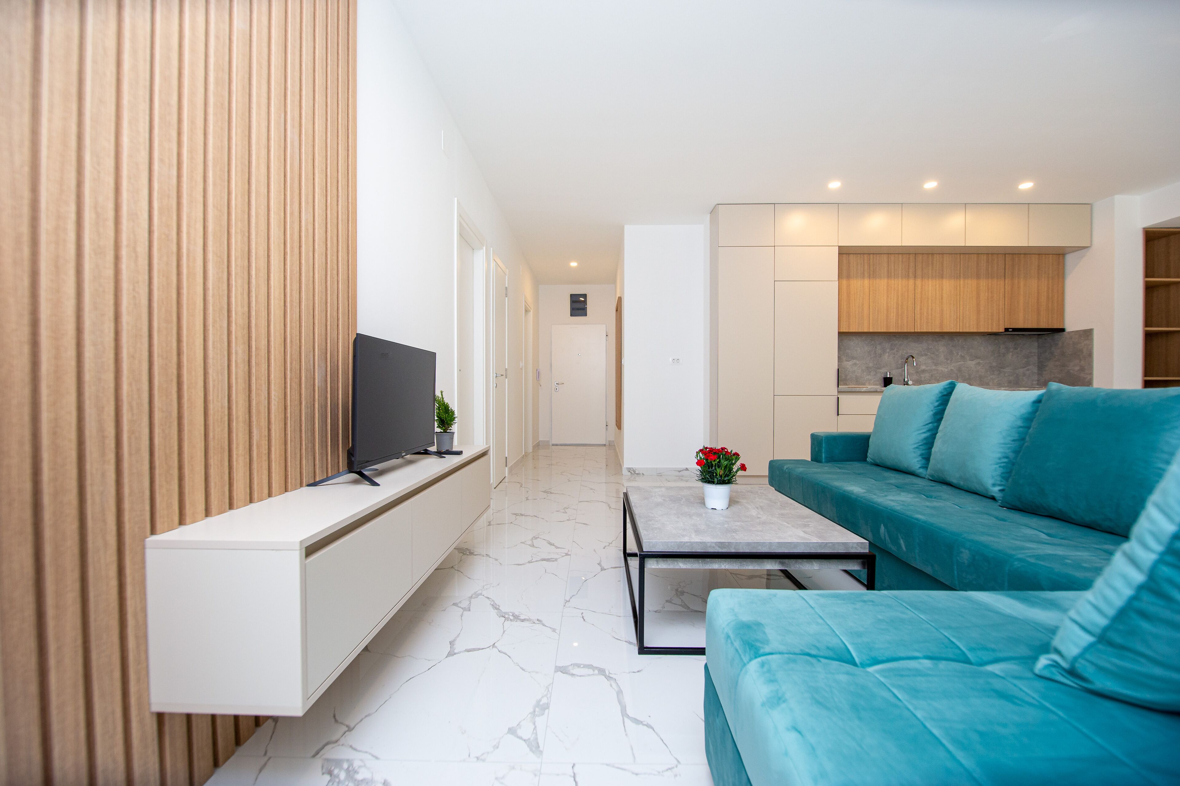 Ein modernes Wohnzimmer mit Flachbildfernseher, einer Couch, einem Couchtisch und einer Küchenzeile im Hintergrund.