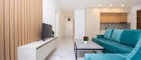 Ein modernes Wohnzimmer mit Flachbildfernseher, einer Couch, einem Couchtisch und einer Küchenzeile im Hintergrund.