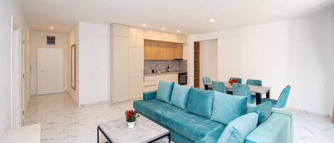 A modern living room with a sectional sofa, a dining area with a table and chairs, and a kitchen in the background.