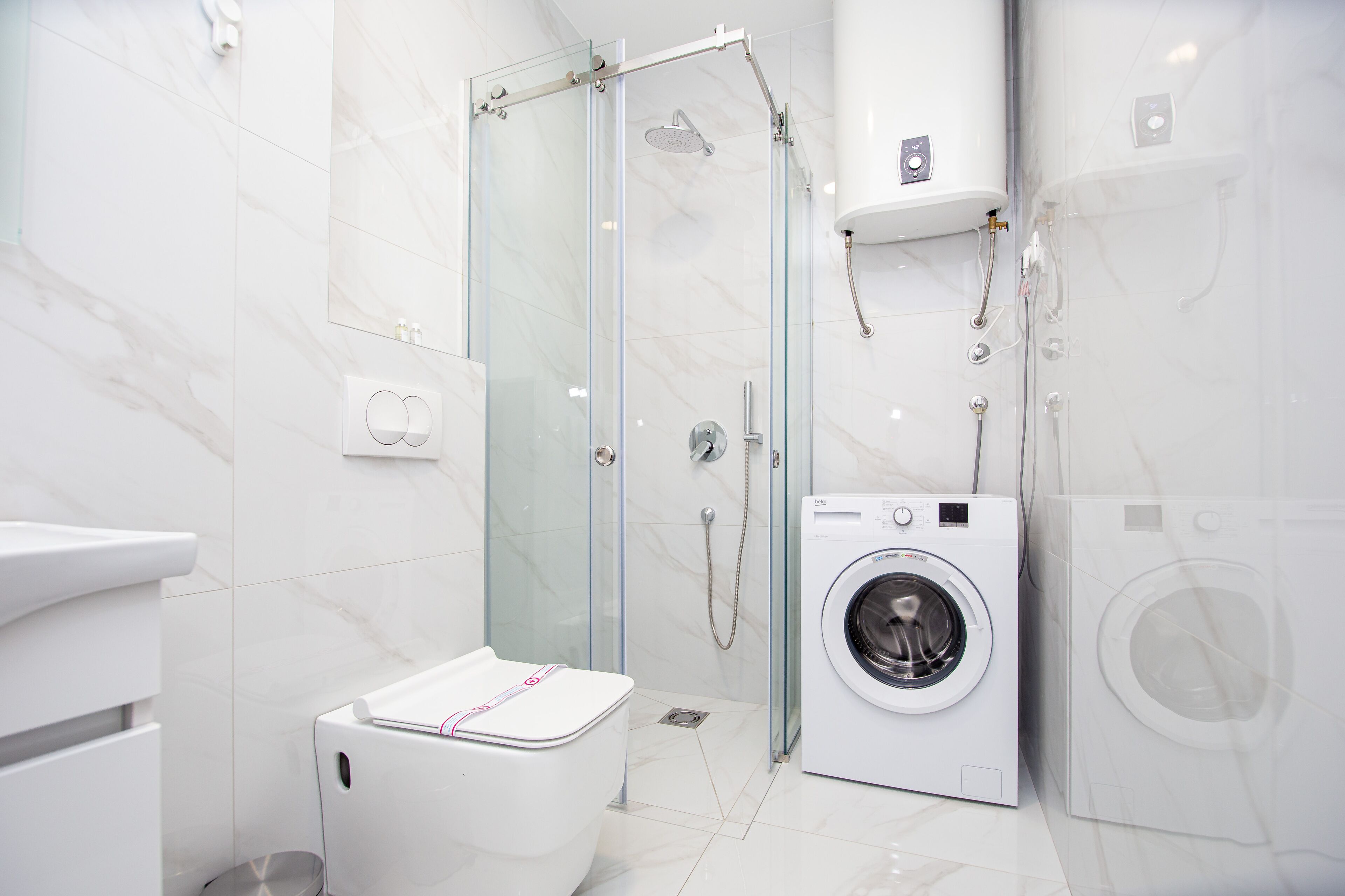 Et moderne badeværelse med glasvæg omkring bruseren, en vaskemaskine og toilet.