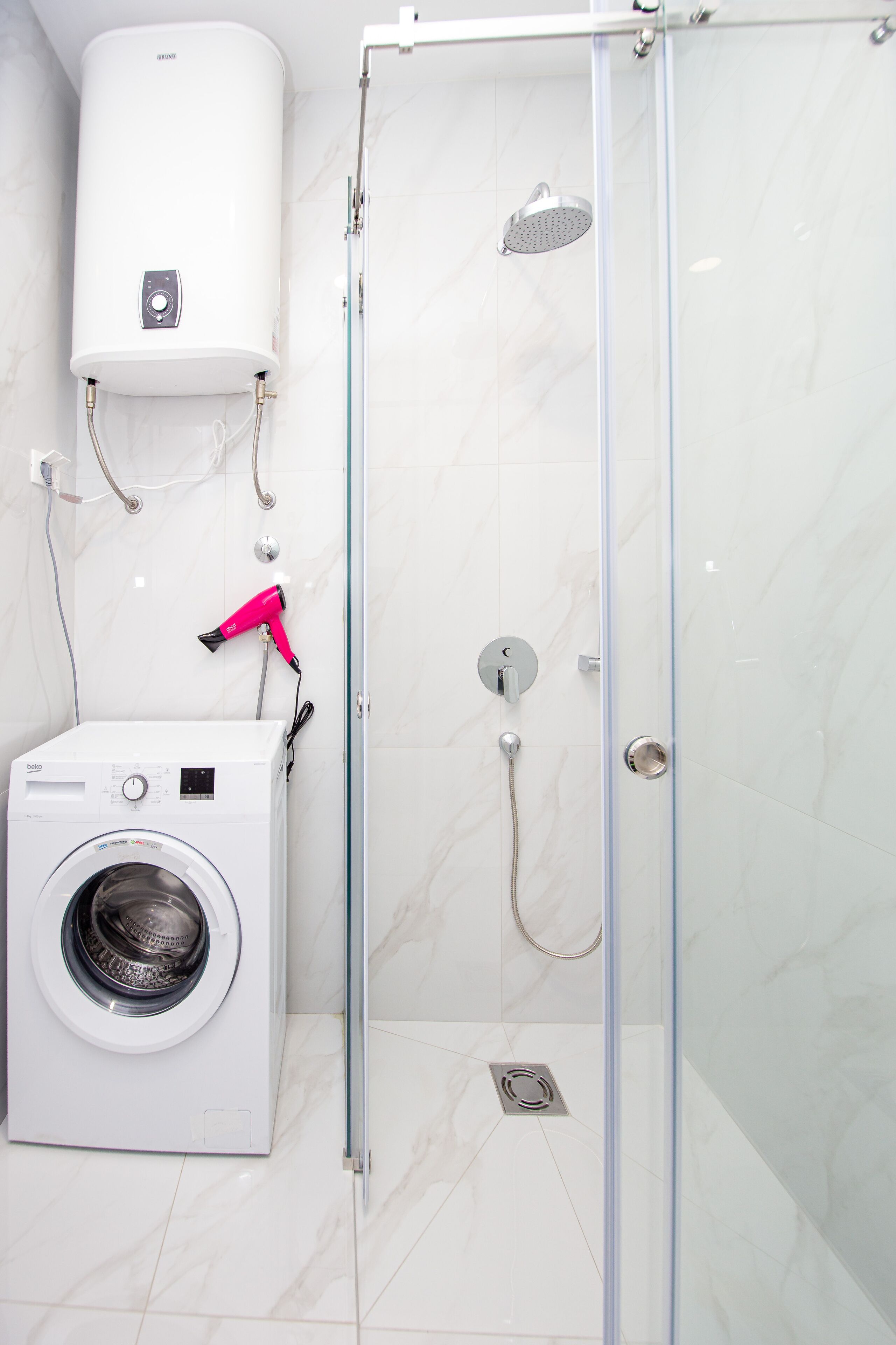 A bathroom with a glass-enclosed shower, a wall-mounted heater, and a front-loading washing machine.