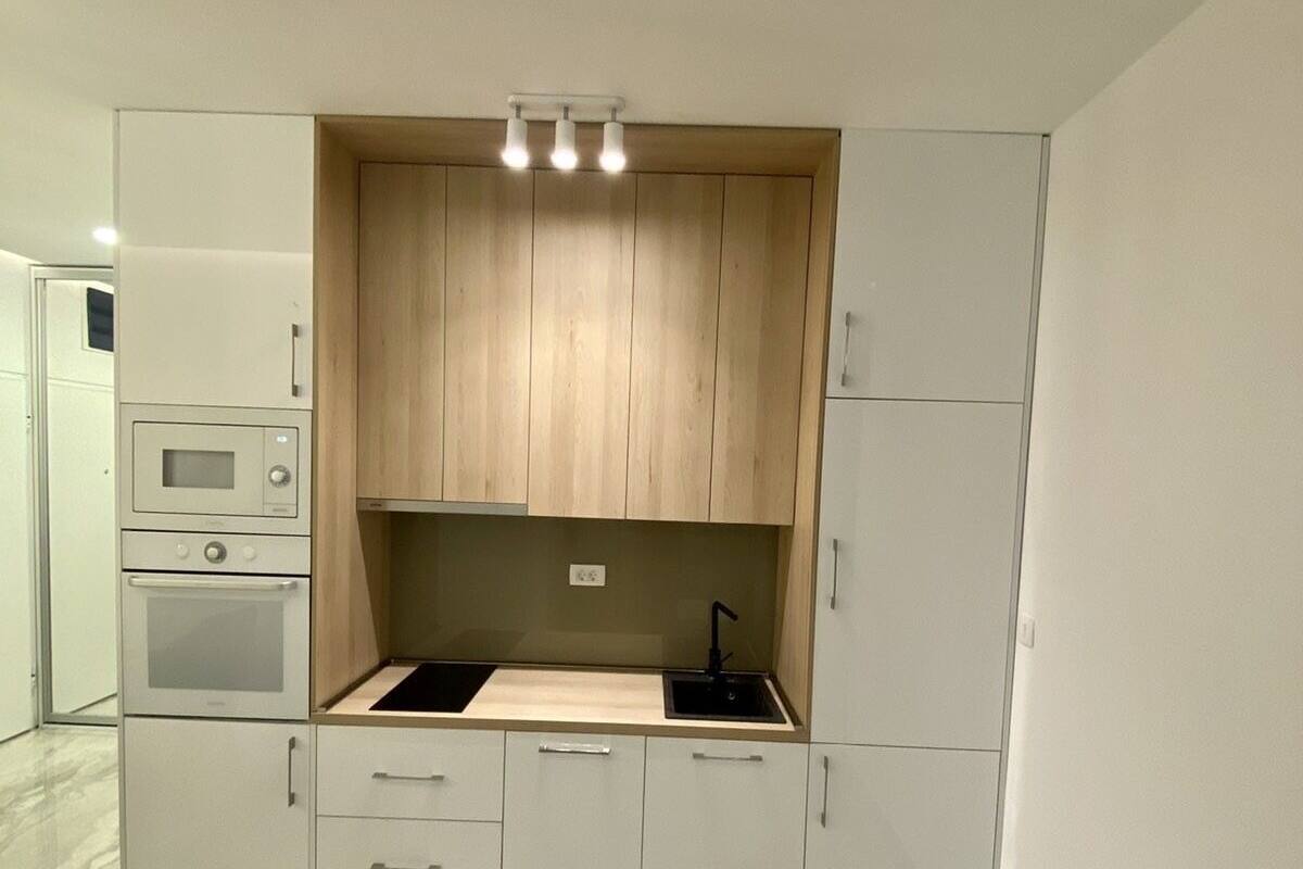 A modern kitchen with built-in appliances, a wooden upper cabinet, and a marble floor.