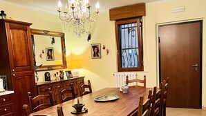 A dining room with a wooden table, chairs, a chandelier, a mirror, and a window with bars. - Villa nestled in the countryside, within walking distance of the sea! (Rodi Garganico, Puglia)
