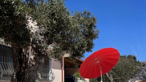 A stone-paved outdoor area with a red umbrella, white chairs, and a tree. - Villa nestled in the countryside, within walking distance of the sea! (Rodi Garganico, Puglia)