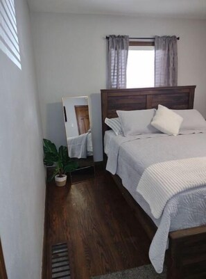 A bedroom with a wooden bed, white bedding, a mirror, and a potted plant.
