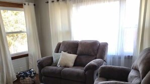 Una sala de estar con un sofá marrón, un tapete gris y una ventana con cortinas translúcidas.