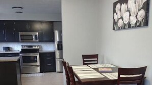 Una cocina moderna con armarios oscuros, electrodomésticos de acero inoxidable y una zona de comedor con mesa y sillas de madera.