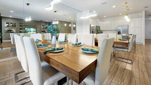 A modern dining area with a wooden table, white chairs, and a large mirror reflecting the space. - Modern 12 BR 11.5 BA, Sleeps 32, 15 mins to Disney (Kissimmee)
