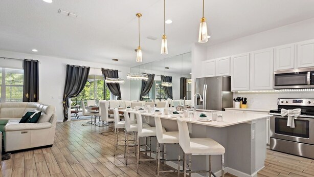 A modern kitchen with white cabinetry, stainless steel appliances, and a central island with bar stools. - Modern 12 BR 11.5 BA, Sleeps 32, 15 mins to Disney (Kissimmee)