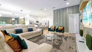 A modern living room with a sofa, armchairs, a coffee table, and a kitchen in the background. - Modern 12 BR 11.5 BA, Sleeps 32, 15 mins to Disney (Kissimmee)