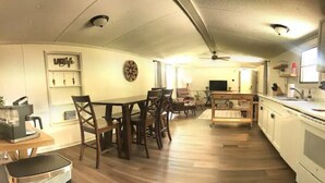 A spacious kitchen with wooden flooring, a dining area with a table and chairs, and a television in the background. - Paradise in the Pines! Your vacation destination! (Hemphill)