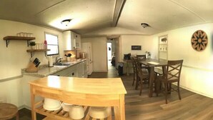 A compact kitchen with wooden cabinets, a central island, and a dartboard on the wall. - Paradise in the Pines! Your vacation destination! (Hemphill)