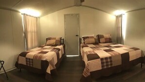 A room with two beds, each with a checkered bedspread, a ceiling fan, and a door in the center. - Paradise in the Pines! Your vacation destination! (Hemphill)