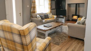 A cozy living room with a sofa, armchair, and coffee table, a fireplace, and a television. - Rock Cottage (Penrith)
