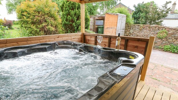 A hot tub with a wooden deck and stone wall in the background. - Rock Cottage (Penrith)