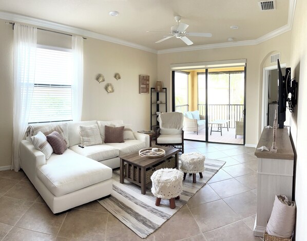 A spacious living room with a white sofa, a wooden coffee table, and a large sliding glass door leading to an outdoor balcony.