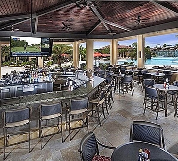 An outdoor bar area with a pool view, bar stools, and a television screen.