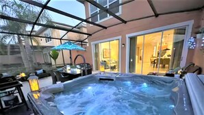 A hot tub in a covered outdoor area with a patio, a dining table, and chairs. - #5763 Luxury Lakefront Priv Spa Pool Disney Epic (Kissimmee)