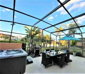 A covered outdoor patio with a table and chairs, a hot tub, and a grill.