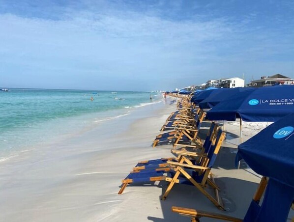 Relax on the beach with comfortable chairs and umbrellas, surrounded by clear blue waters and a sandy shore.