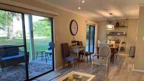 A spacious living area with a large sliding glass door leading to a patio, a dining area with a table and chairs, and a kitchen area with a sign reading "BEACH HOUSE". - Destin, FL. Escape to Mirarmar Beach on Seascape resort (Miramar Beach)