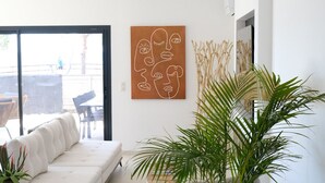 A modern living room with a white sofa, a large window, and a wall-mounted abstract art piece.