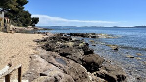 A rocky beach with a wooden bench and a building with graffiti.