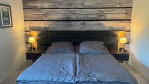 A bed with a headboard made of wooden planks, two bedside tables with lamps, and a framed picture on the wall. - Quiet apartment with a great view (Wehretal)