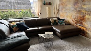 A modern living room with a sectional sofa, a round coffee table, and a large abstract painting on the wall. - Quiet apartment with a great view (Wehretal)