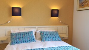 A bed with a white headboard and two patterned pillows, two wall-mounted lamps, and a framed picture on the wall. - Maison de Campagne Proche mer - 5 Voyageurs (Regnéville-sur-Mer)