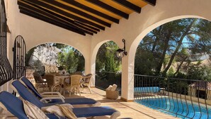 Ein überdachter Außenbereich mit Liegestühlen, einem Pool und einem Tisch mit Stühlen.