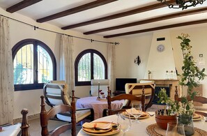 A dining room with a fireplace, two large arched windows, and a dining table set with plates, glasses, and a vase of flowers. - Villa RODRIGANDA in Moraira – 3 bedrooms, private pool, 700 metres from El Portet beach, air conditioning and Wi-Fi (Moraira)