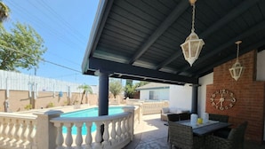 Un patio exterior con piscina, una mesa con sillas y un reloj en la pared.