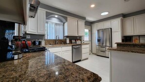 Una cocina moderna con encimeras de granito, electrodomésticos de acero inoxidable y armarios blancos.