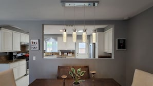 Un comedor con una mesa de madera, sillas, una planta en maceta y lámparas colgantes.