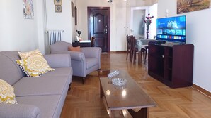 Ein Wohnzimmer mit Sofa, Couchtisch, Fernseher, Essbereich und Kunstwerken an den Wänden.