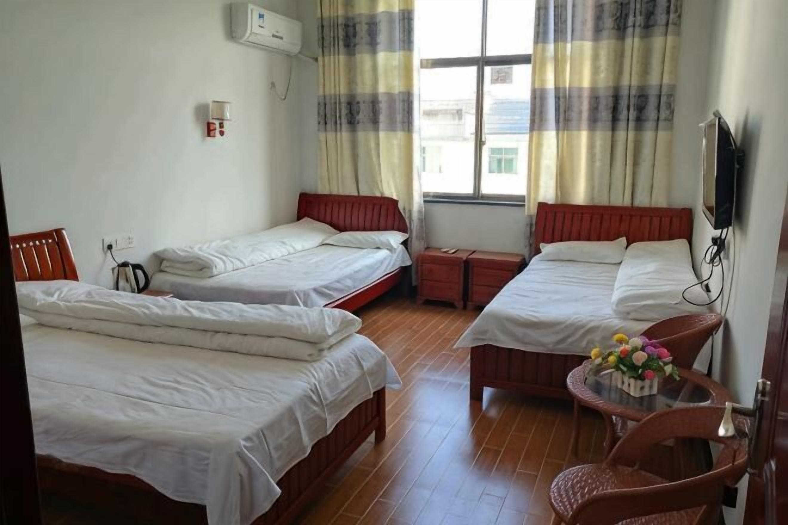 A room with two beds, a small table with flowers, a chair, and a TV mounted on the wall.