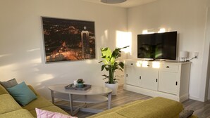 Ein modernes Wohnzimmer mit einer Couch, einem Couchtisch, einer Topfpflanze, einem Flachbildfernseher und einem Schrank.