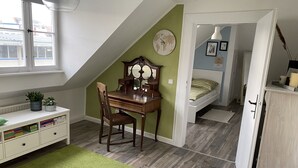 Ein Zimmer mit schrägem Dach, einem Schreibtisch mit Stuhl, einem Bett und einer Heizung.