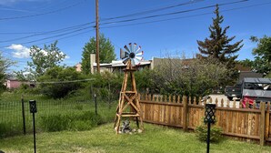 Un jardin avec un moulin à vent, une clôture en bois et un véhicule garé à proximité.