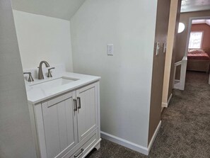 A bathroom with a white vanity, a sink, and a mirror. There is a door leading to another room with a bed. - Steps from restaurants and the historic Stockman’s Bar and Grill. (Walden)