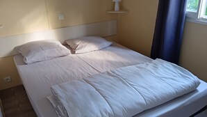 A single bed with white bedding, a bedside table with a lamp, and a window with curtains. - Bungalow in a comfortable 3-star campsite. Accepted animals. (Argelès-sur-Mer)