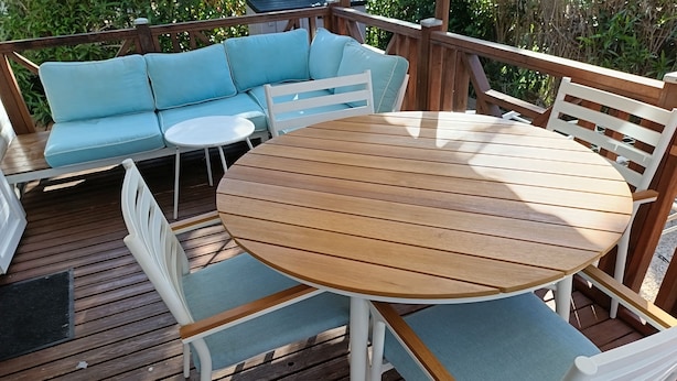 A wooden deck with a round table and chairs, a light blue sofa, and a white railing. - Bungalow in a comfortable 3-star campsite. Accepted animals. (Argelès-sur-Mer)