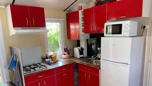 A compact kitchen with red cabinets, a white refrigerator, a microwave, and a gas stove. - Bungalow in a comfortable 3-star campsite. Accepted animals. (Argelès-sur-Mer)
