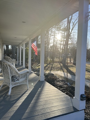 A covered porch with white columns, a wicker chair, and an American flag.