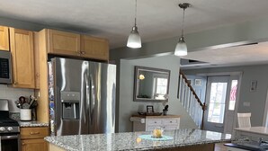 Eine moderne Küche mit Edelstahl-Kühlschrank, Holzschränken, Granit-Arbeitsplatten und einer Bar mit Hockern.