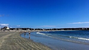 Ein Strand mit Häusern im Hintergrund und Menschen, die am Ufer entlanggehen.